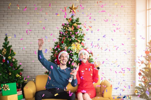 man and woman wearing santa hats sitting on sofa popping a 3183392
